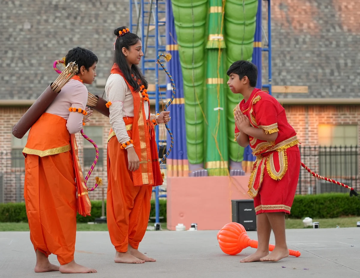 Young performers in traditional costumes presenting a scene with a bow and mace.