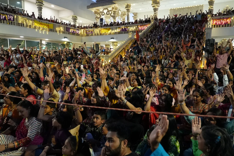 A large temple gathering raising their hands in celebration across the courtyard and balconies.