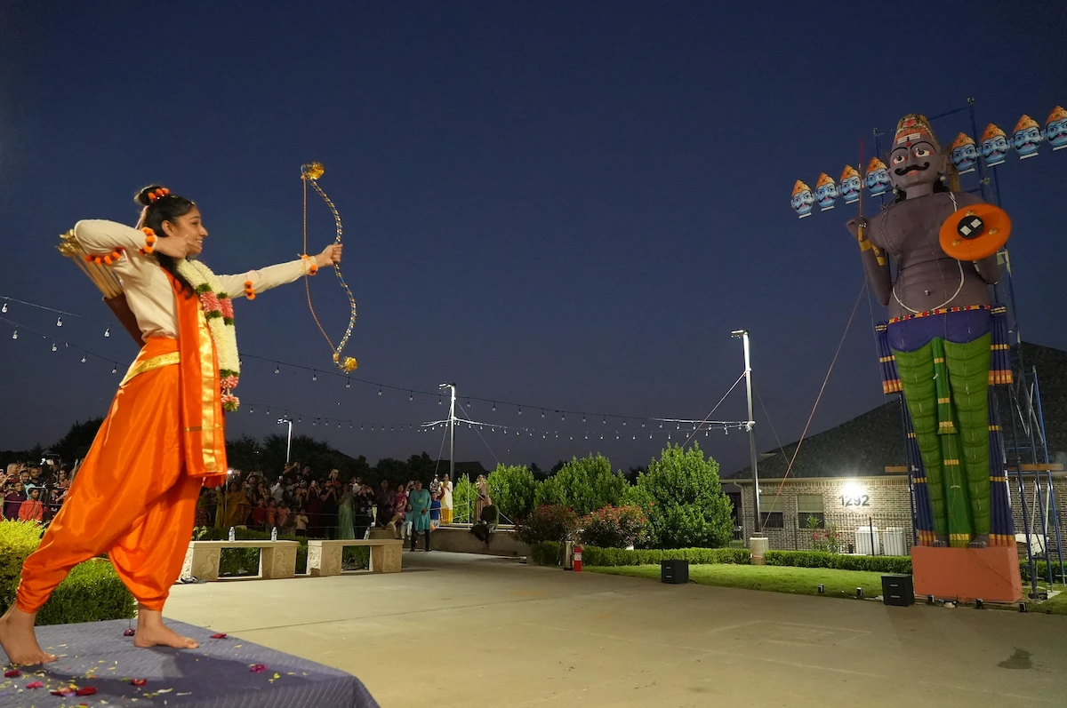 A young performer drawing a bow toward the Ravan effigy at dusk.