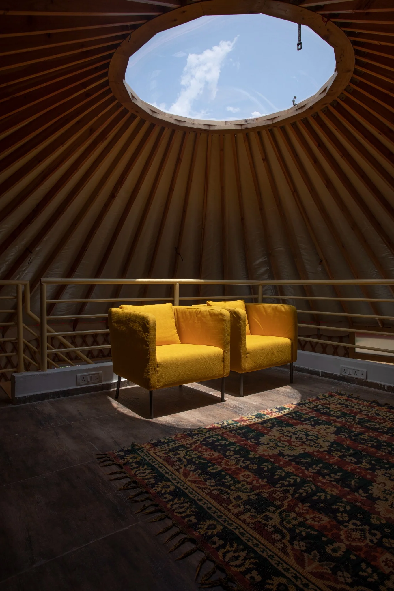 Yellow armchair under circular skylight in wooden yurt-like interior