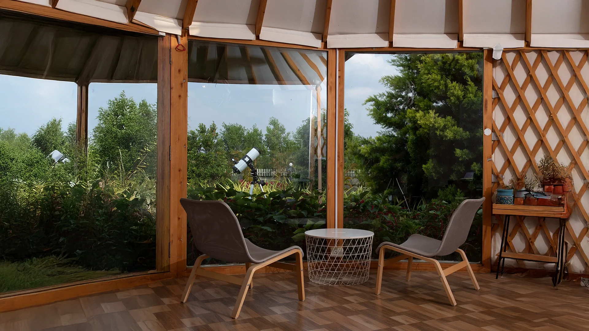 Cozy greenhouse interior with chairs, wire table, and lush garden view