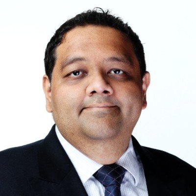 Portrait of a man with dark hair wearing a dark suit, white shirt, and patterned tie against a white background.