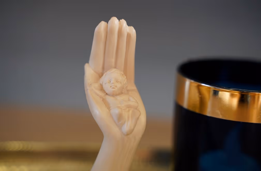 Bildet viser en håndlaget trefigur med Jesus-barnet liggende i en hånd
