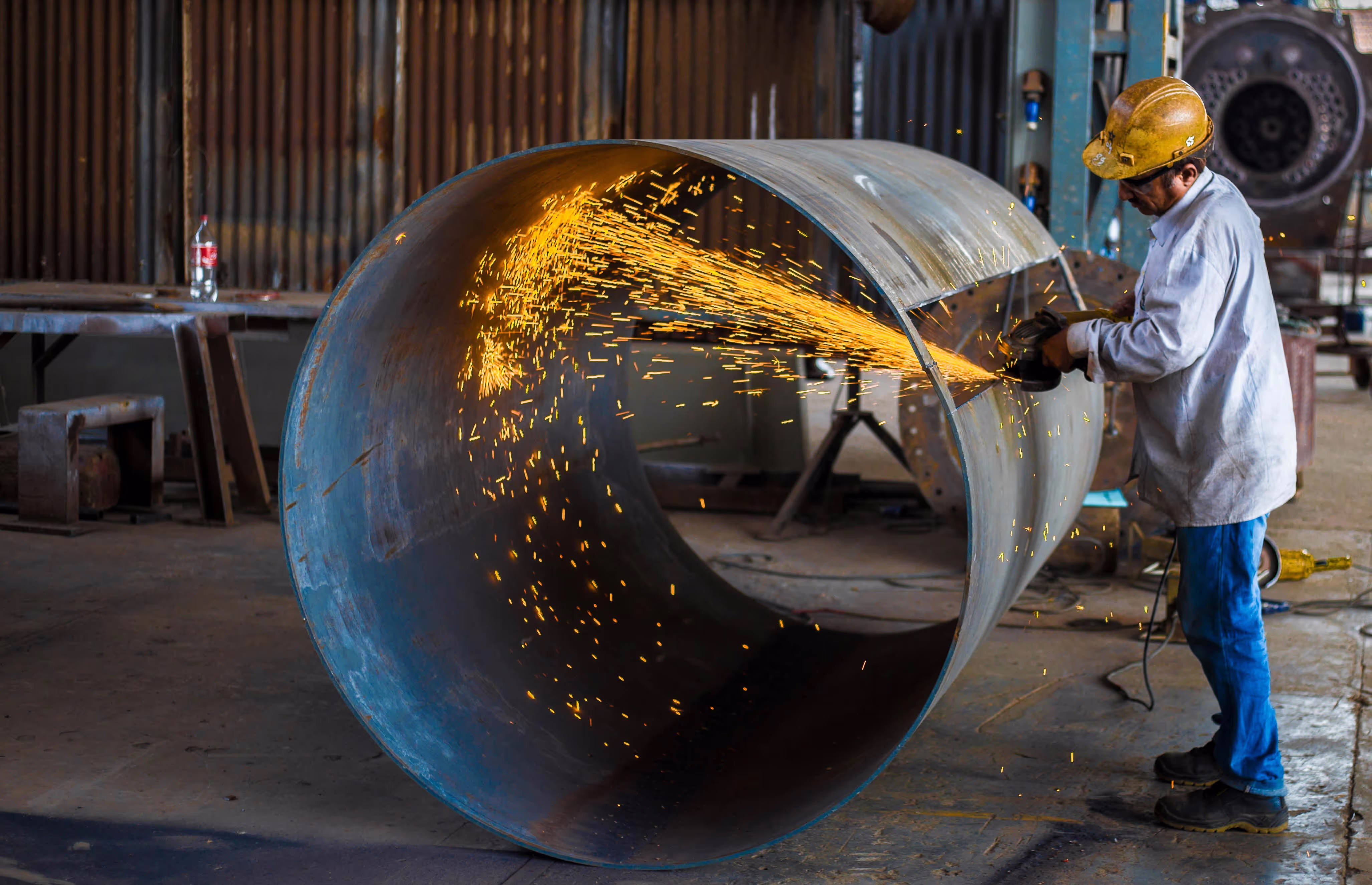 Worker using a cutting torch on a large spherical tank.
