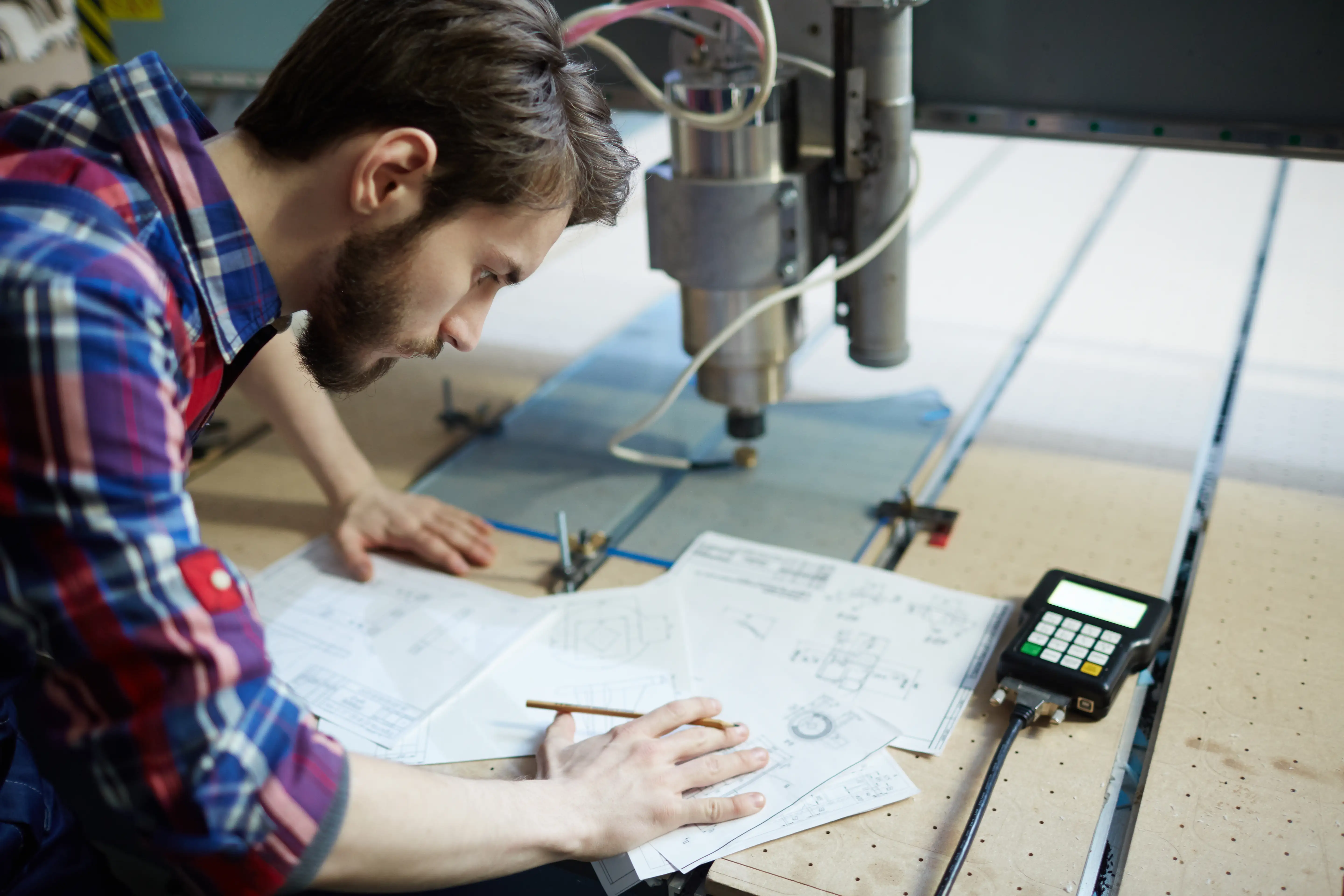 Engineer working with technical drawings and a CNC machine in a workshop.