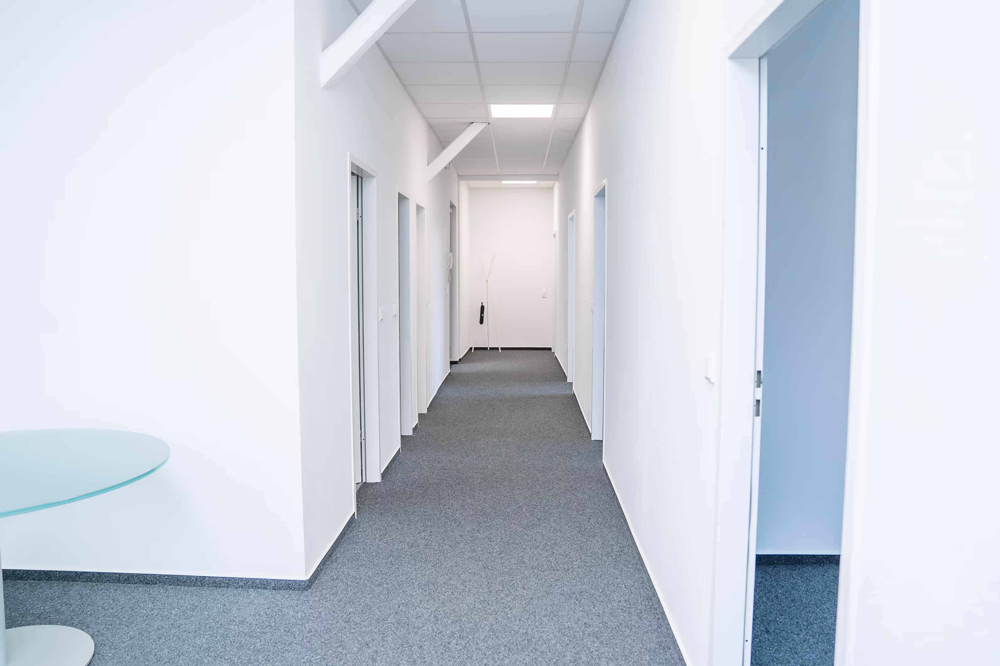 Moderner, heller Büroflur bei PG digital mit weißen Wänden, grauem Teppichboden und mehreren Bürotüren – aufgeräumt, freundlich und einladend.