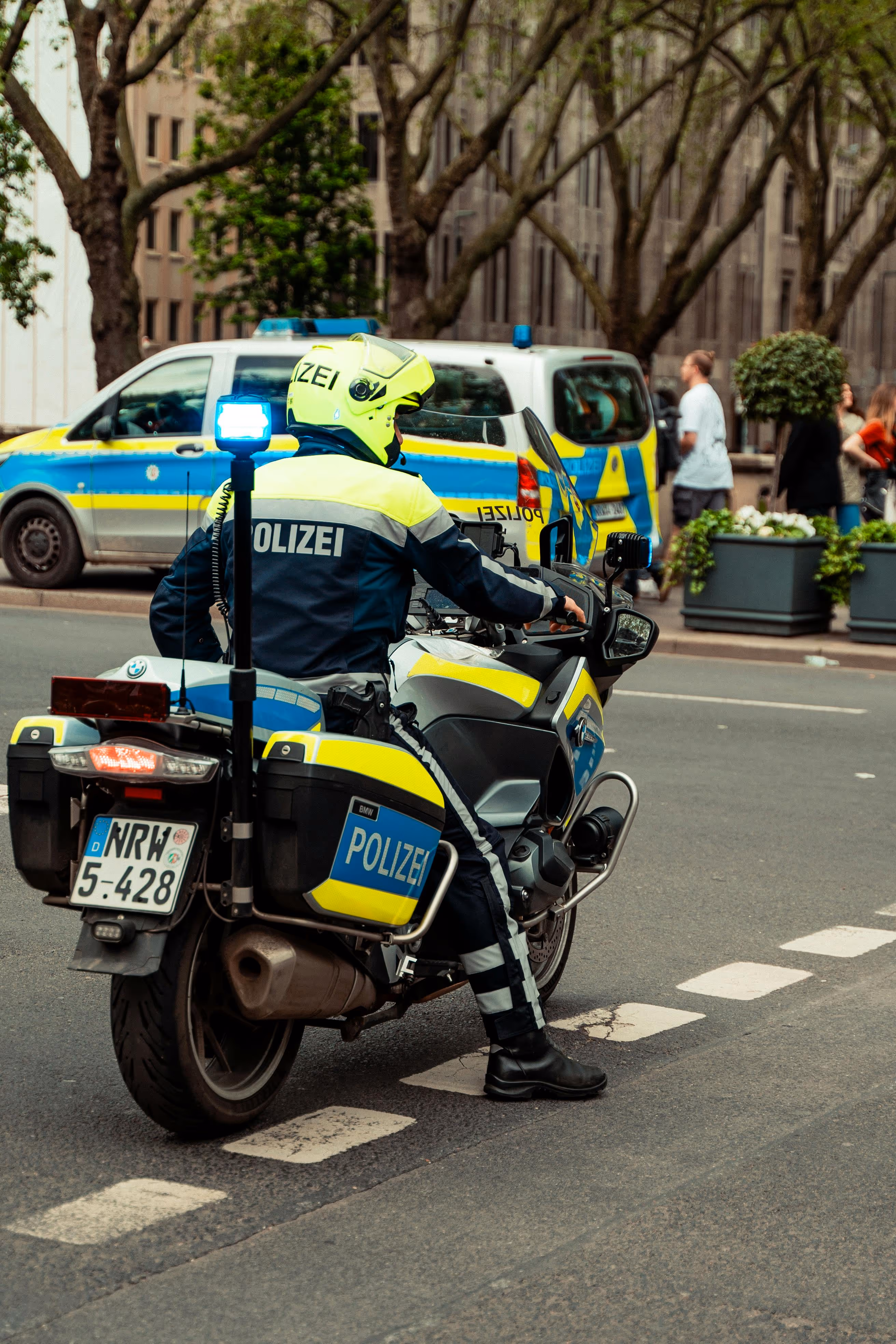 Polizeibeamter in Schutzhelm auf einem Motorrad mit Blaulicht in einer städtischen Umgebung.
