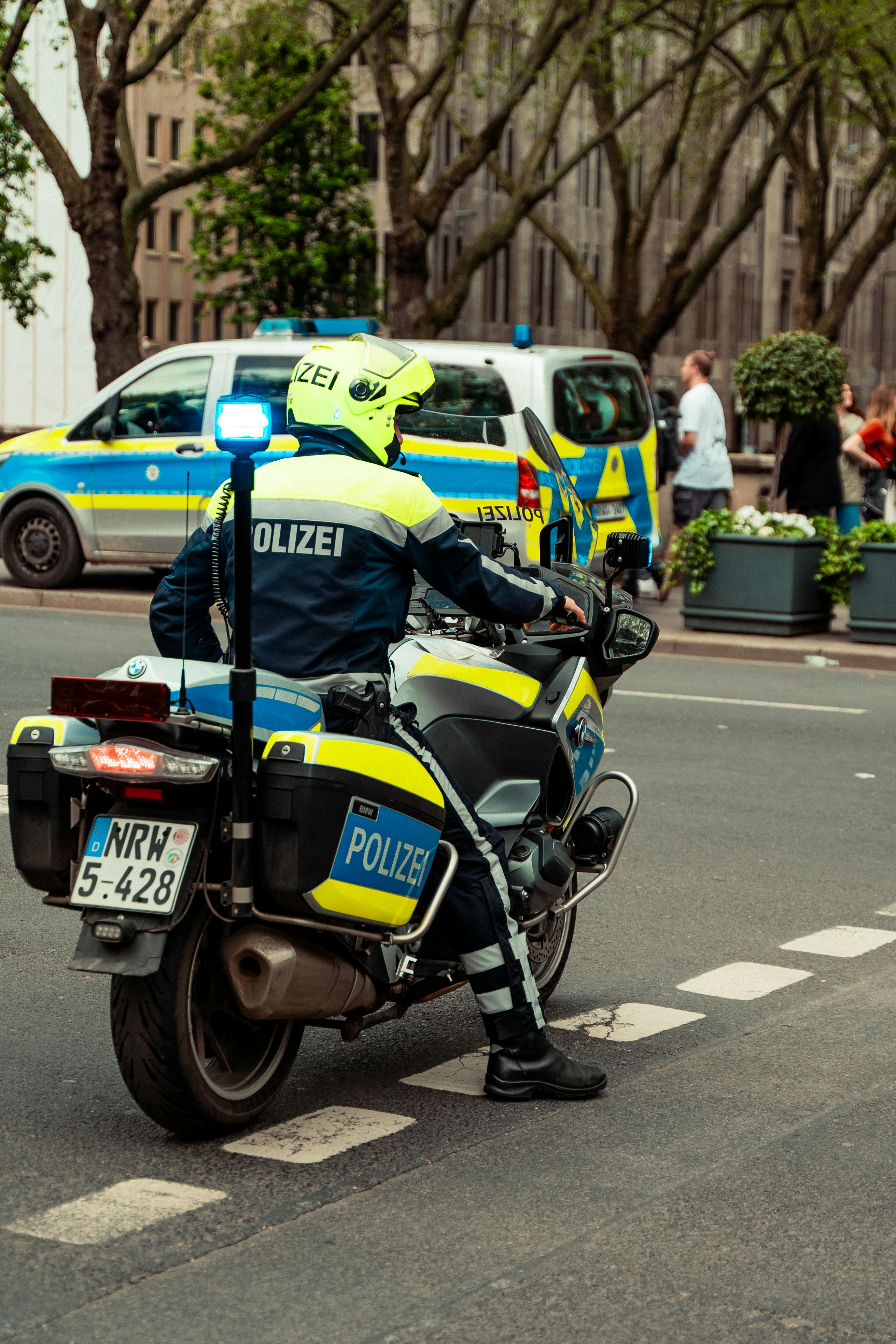 Polizeibeamter in Schutzhelm auf einem Motorrad mit Blaulicht in einer städtischen Umgebung.