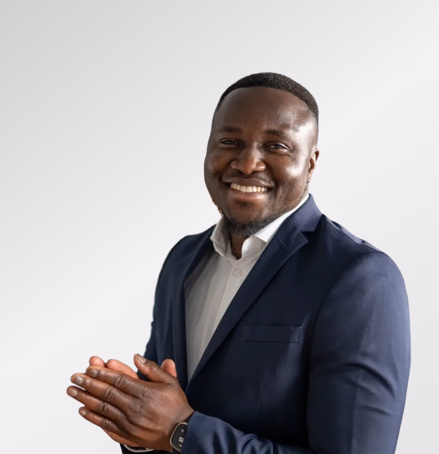 Lächelnder Mann in weißem Hemd und dunklem Sakko, der die Handflächen aneinanderlegt.