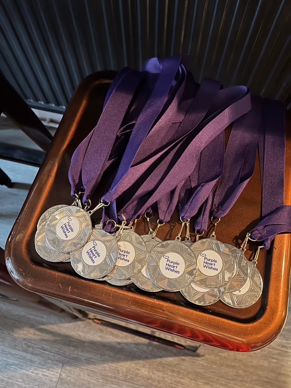 Silver medals with purple ribbons laying on a wooden surface, each medal displaying 'Purple Heart Wishes'.