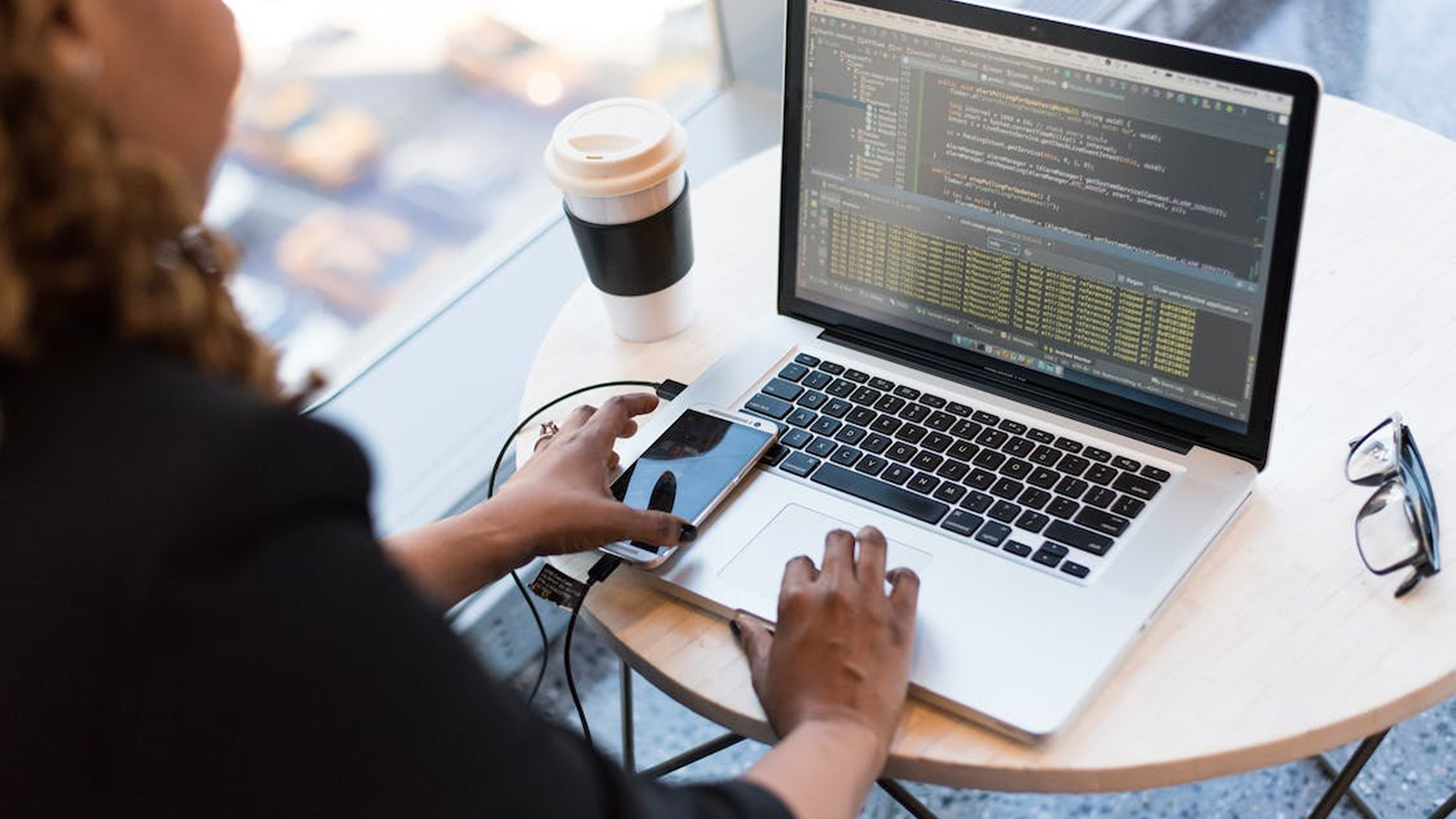 Developer working on a laptop with a phone and coffee
