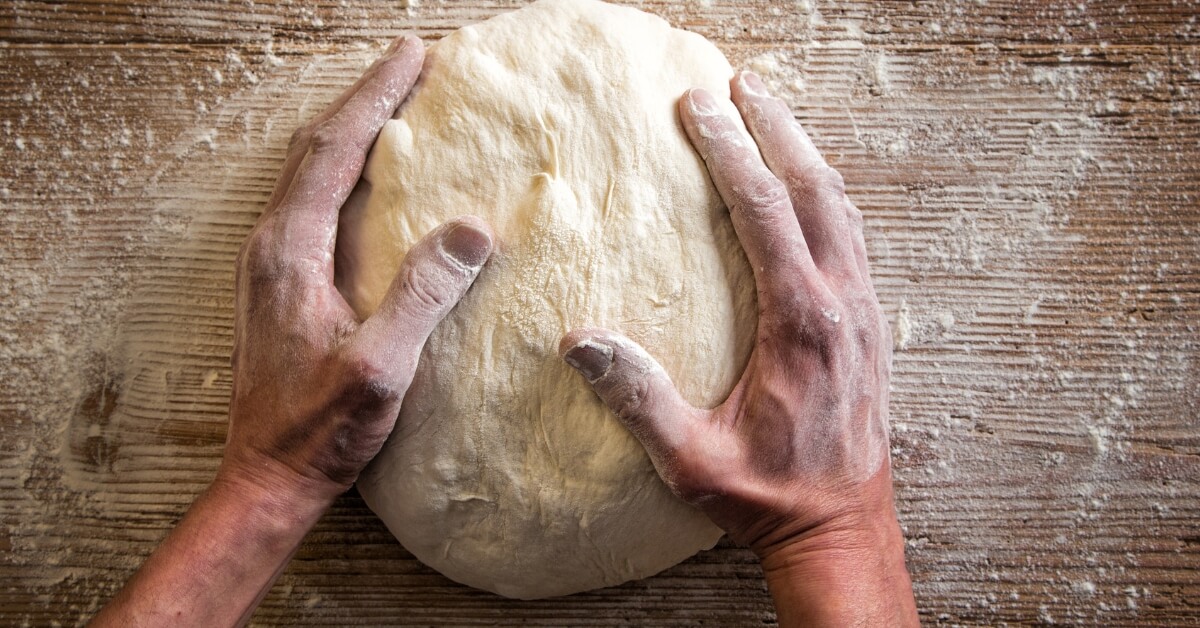 Mains d’un pizzaiolo façonnant une pâte à pizza artisanale sur un plan de travail fariné