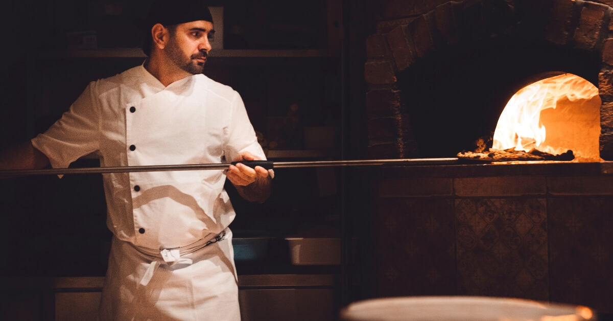 Pizzaiolo en tenue blanche enfournant une pizza dans un four à bois traditionnel