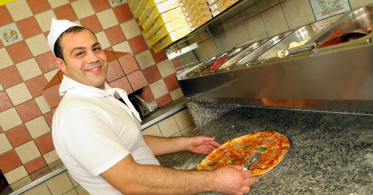 Pizzaiolo souriant présentant une pizza cuite au four dans une pizzeria traditionnelle