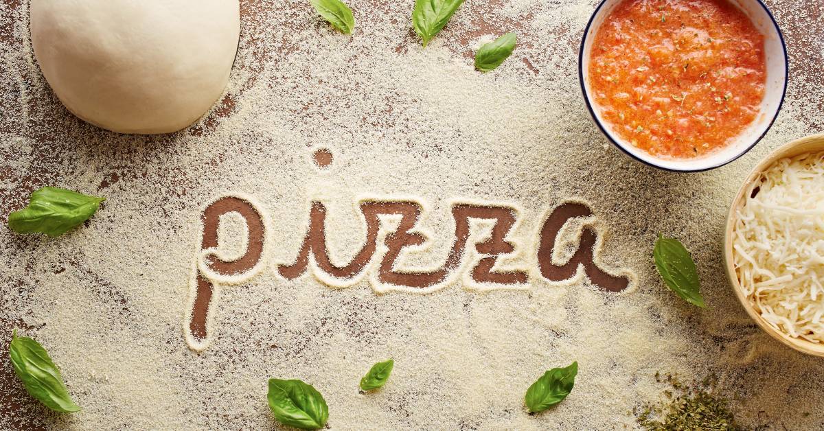 Semoule de blé sur plan de travail avec pâte, sauce tomate et basilic – préparation d’une pizza maison croustillante.