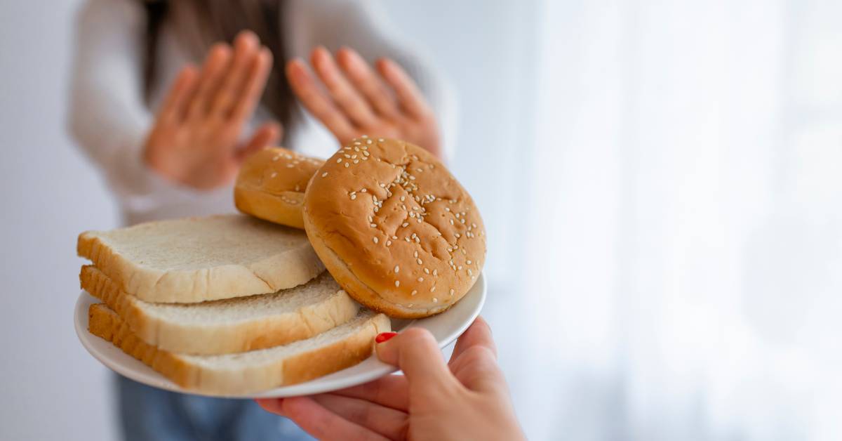 Femme intolérante au gluten refusant du pain et des burgers, symbole des troubles liés à la consommation de gluten.