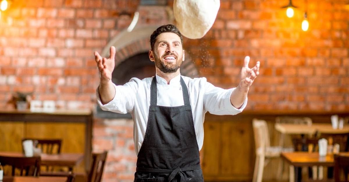 Pizzaiolo expert lançant une pâte à pizza en l'air dans une pizzeria traditionnelle, ambiance conviviale
