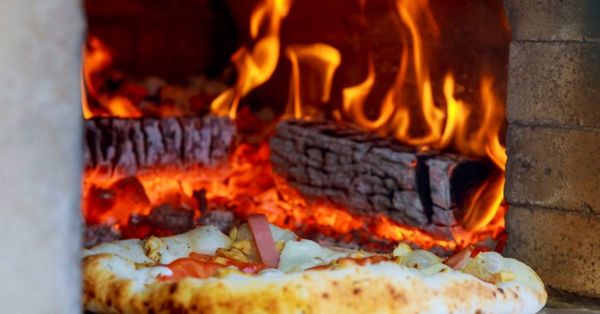 Pizza cuisant dans un four à bois traditionnel avec flammes vives, ambiance artisanale