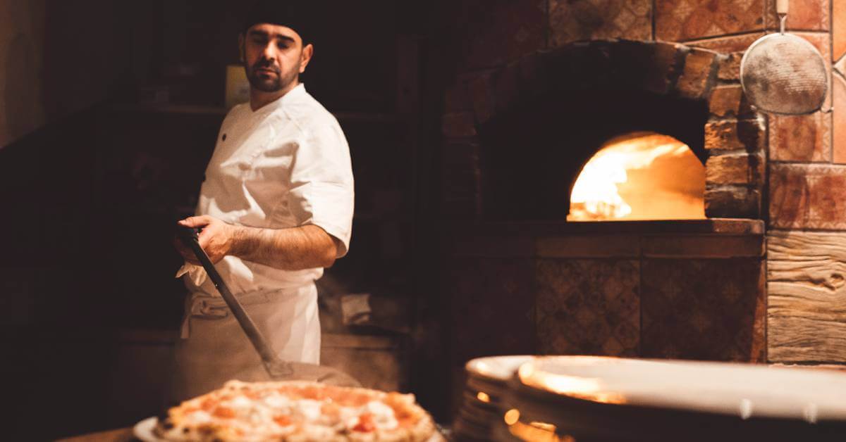 Pizzaiolo devant un four à bois en train d’enfourner une pizza