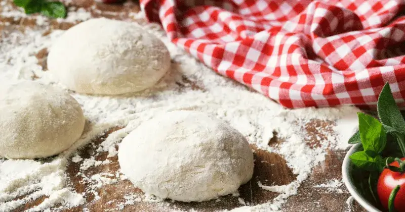Pâtons de pizza maison farinés sur un plan de travail avant fermentation et façonnage de la pizza.