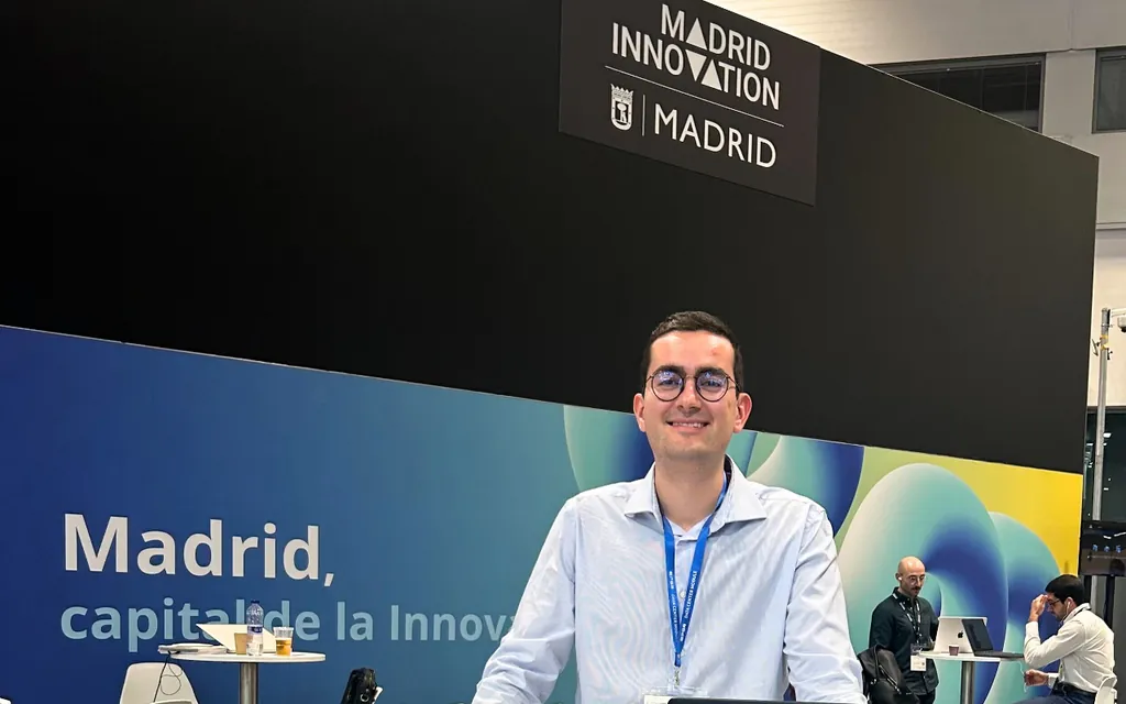 Man with glasses and badge standing with arms crossed in front of Madrid Innovation event signage.
