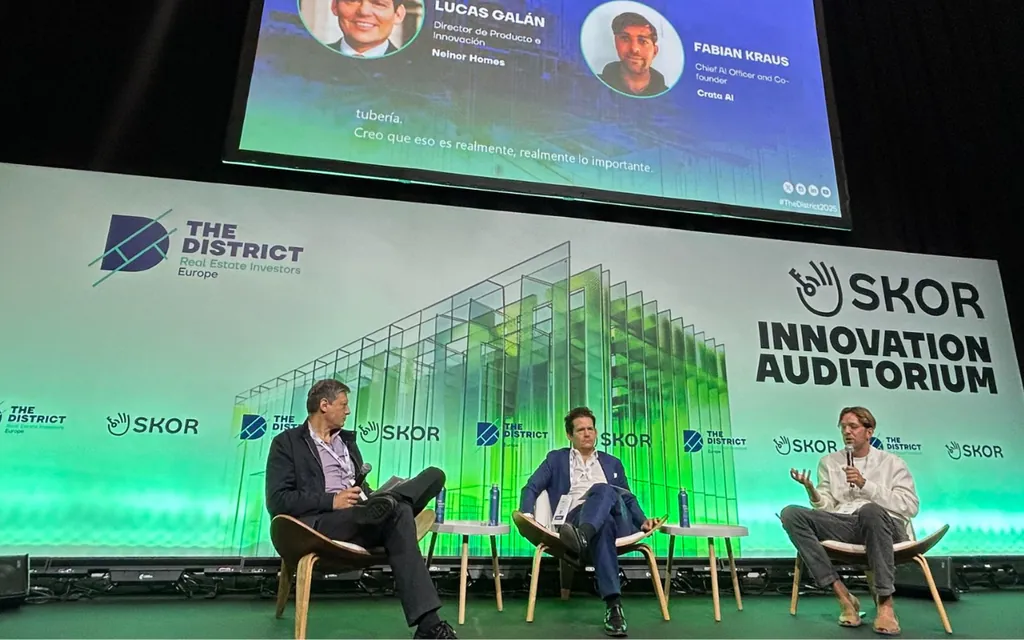 Three men seated on stage chairs in a panel discussion at The District SKOR Innovation Auditorium.