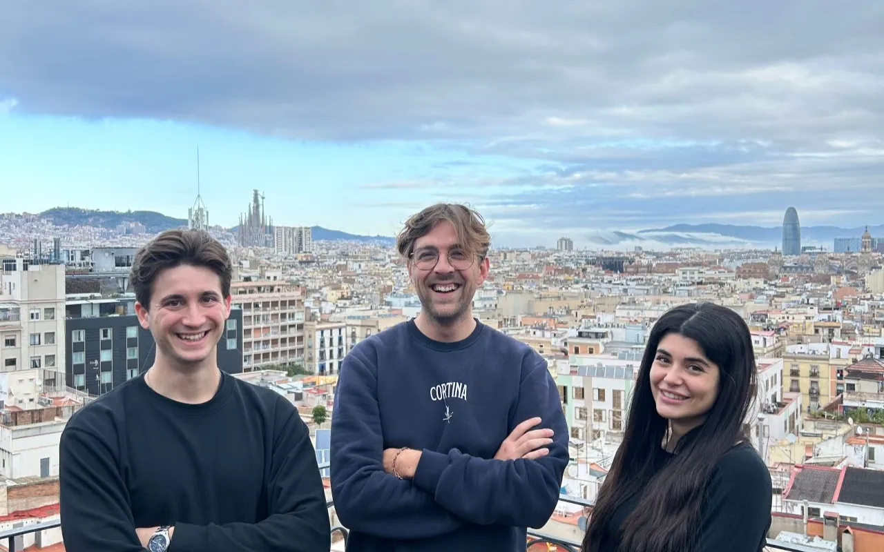 Three young adults smiling with arms crossed overlooking a cityscape with cloudy sky.
