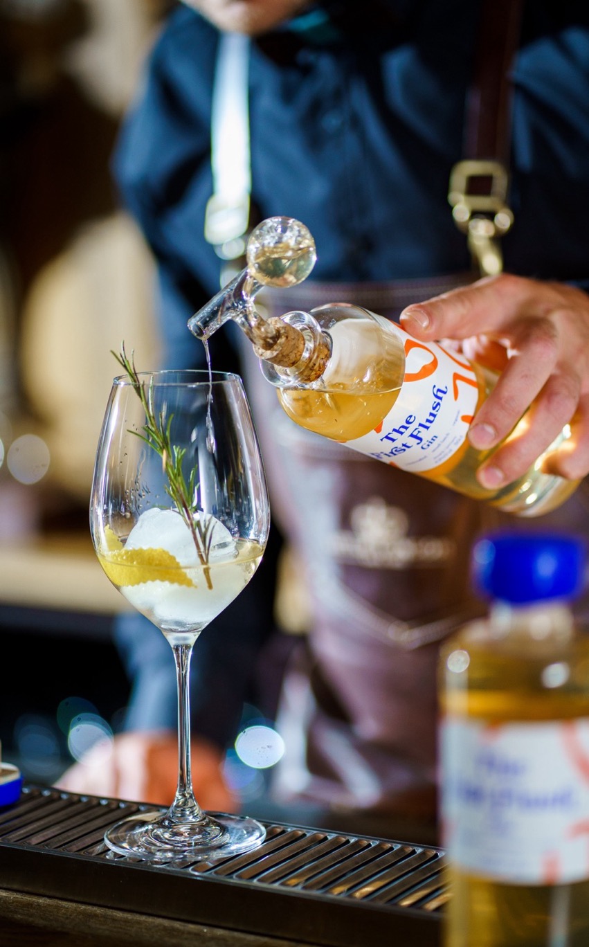 Close Up eines Barkeepers, der eine 50cl First Flush Gin Flasche mit Glaskugelportionierer in der Hand hat und dabei ist Gin in ein Glas zu schenken