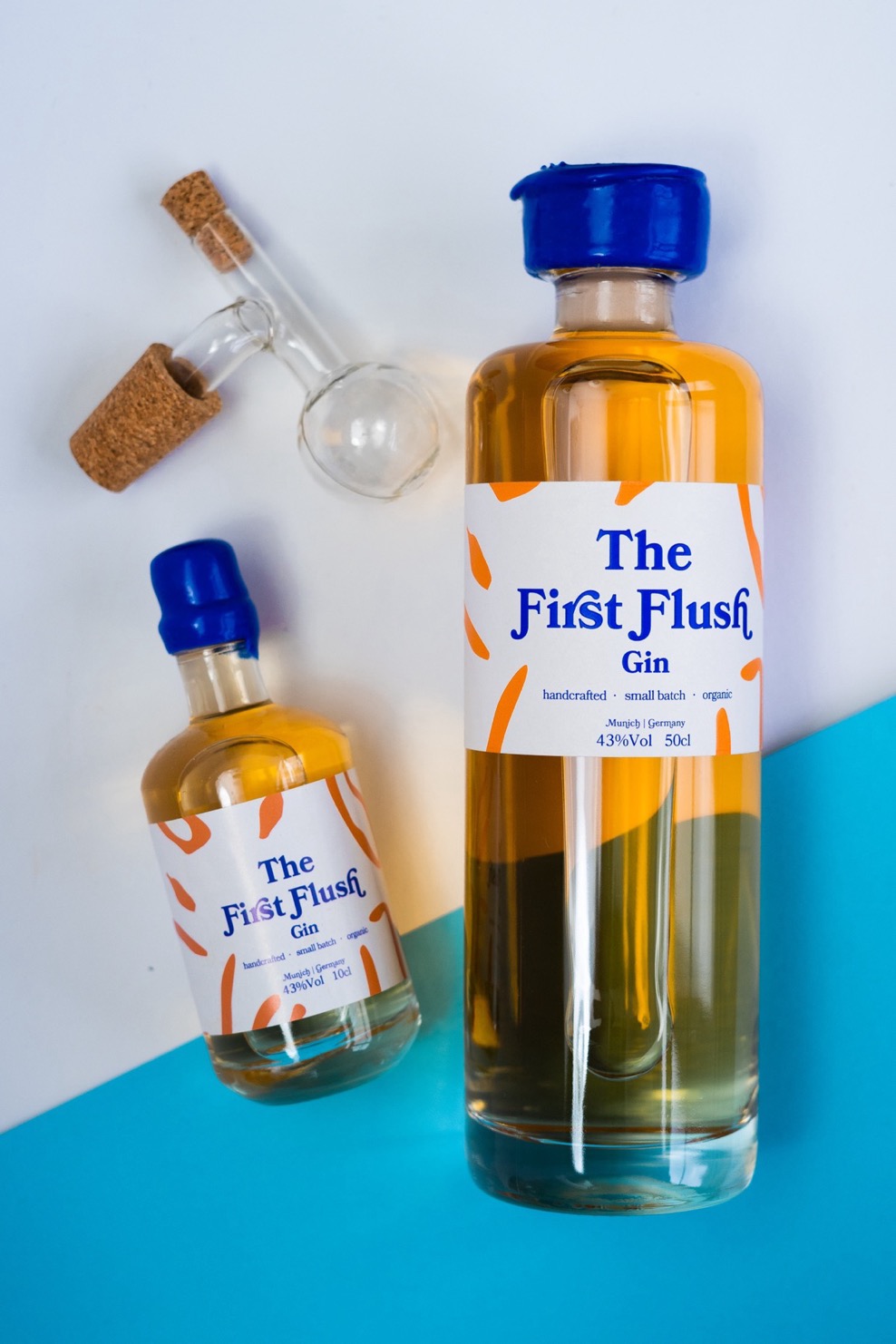 Flasche 10cl First Flush Gin, Flasche 50cl First Flush Gin und 2cl Glaskugelportioniererer auf einen Fotohintergrund in weiß und hellem blau