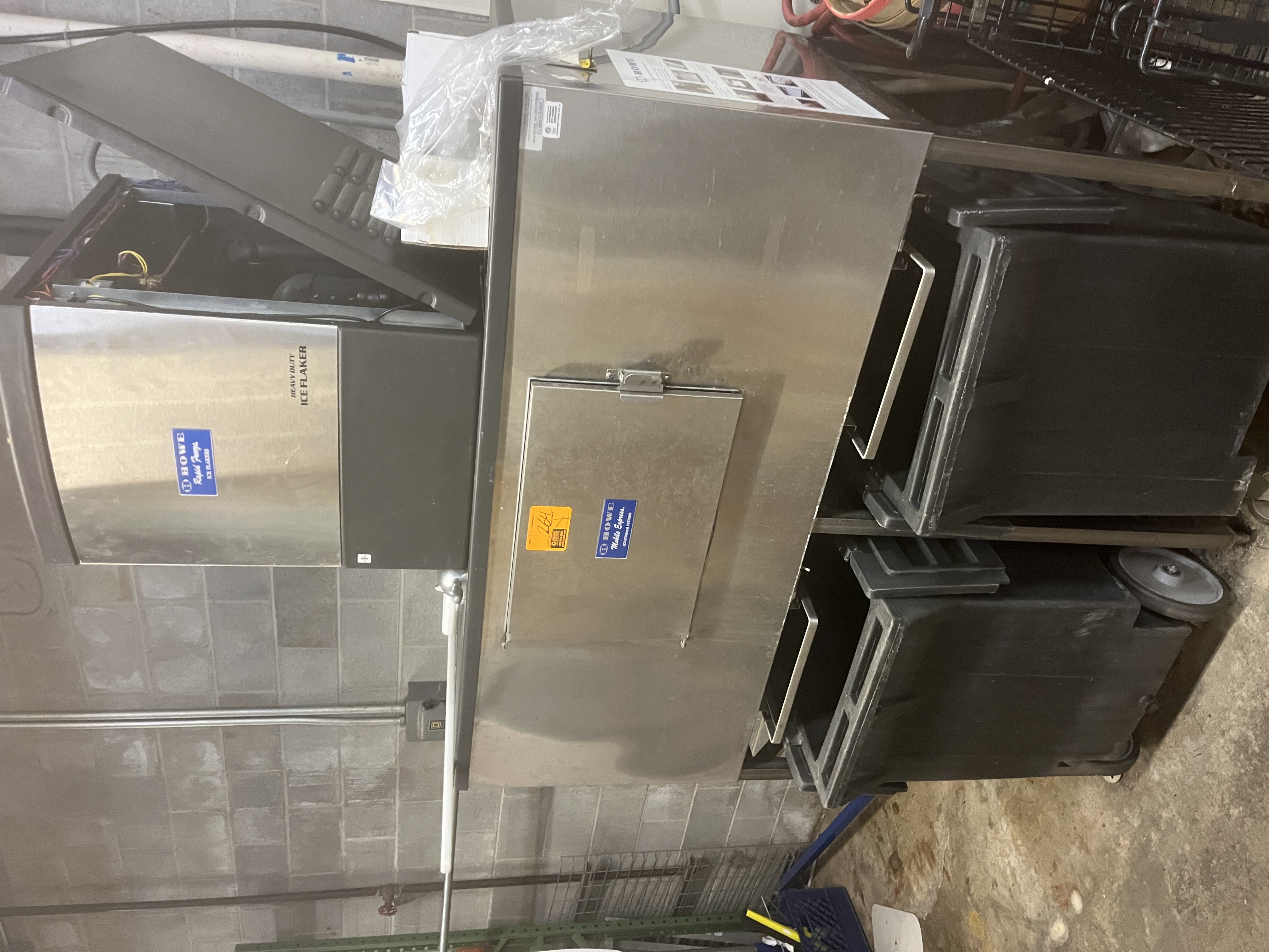 Commercial Howe ice flaker with stainless steel ice bin in a grocery store backroom. Industrial ice machine available from Mid-America Store Fixtures.
