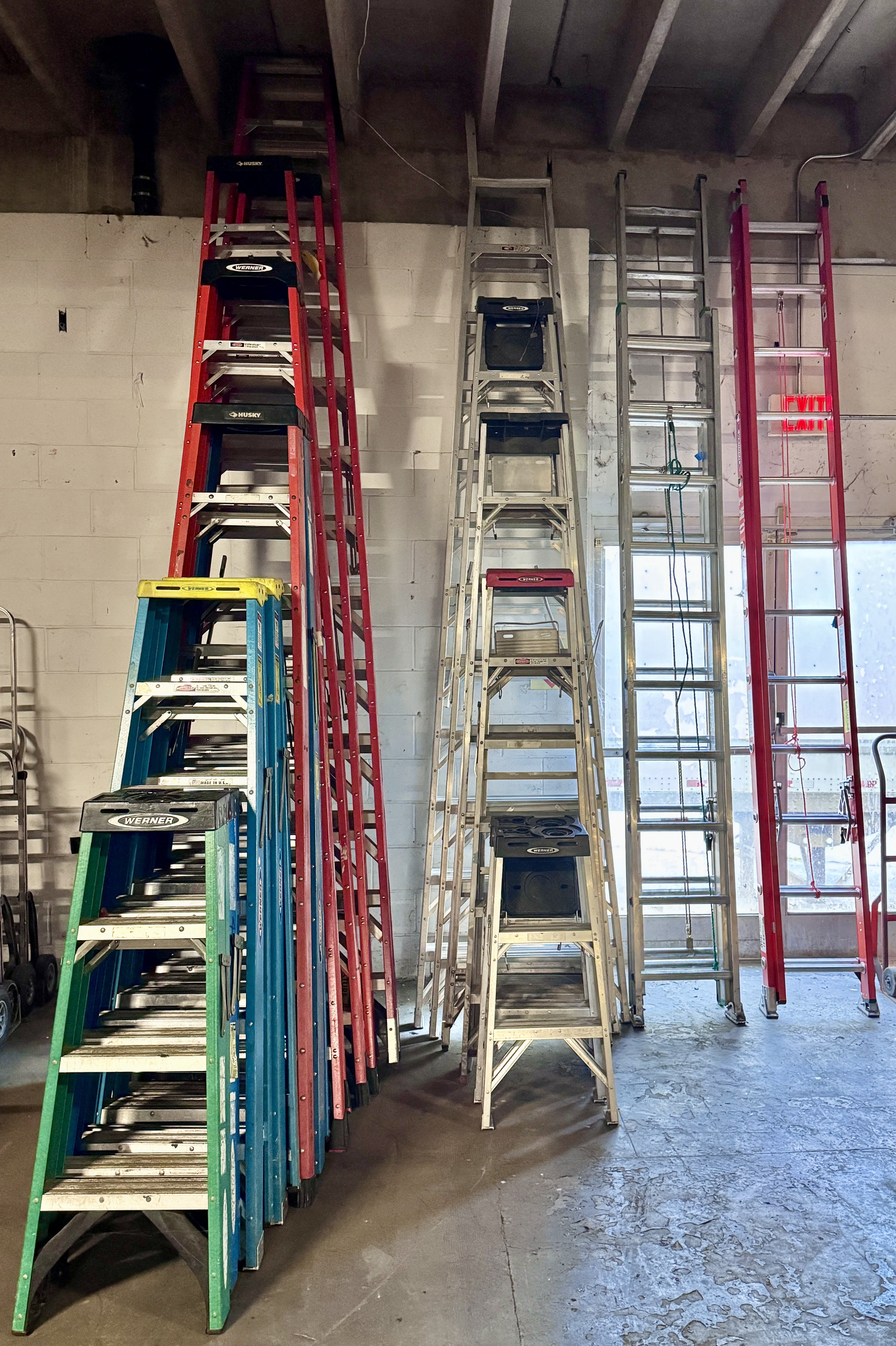 Mixed inventory of tall fiberglass and aluminum A-frame ladders and step ladders ideal for retail backrooms, warehouses, and facility maintenance. Commercial ladders available from Mid-America Store Fixtures.