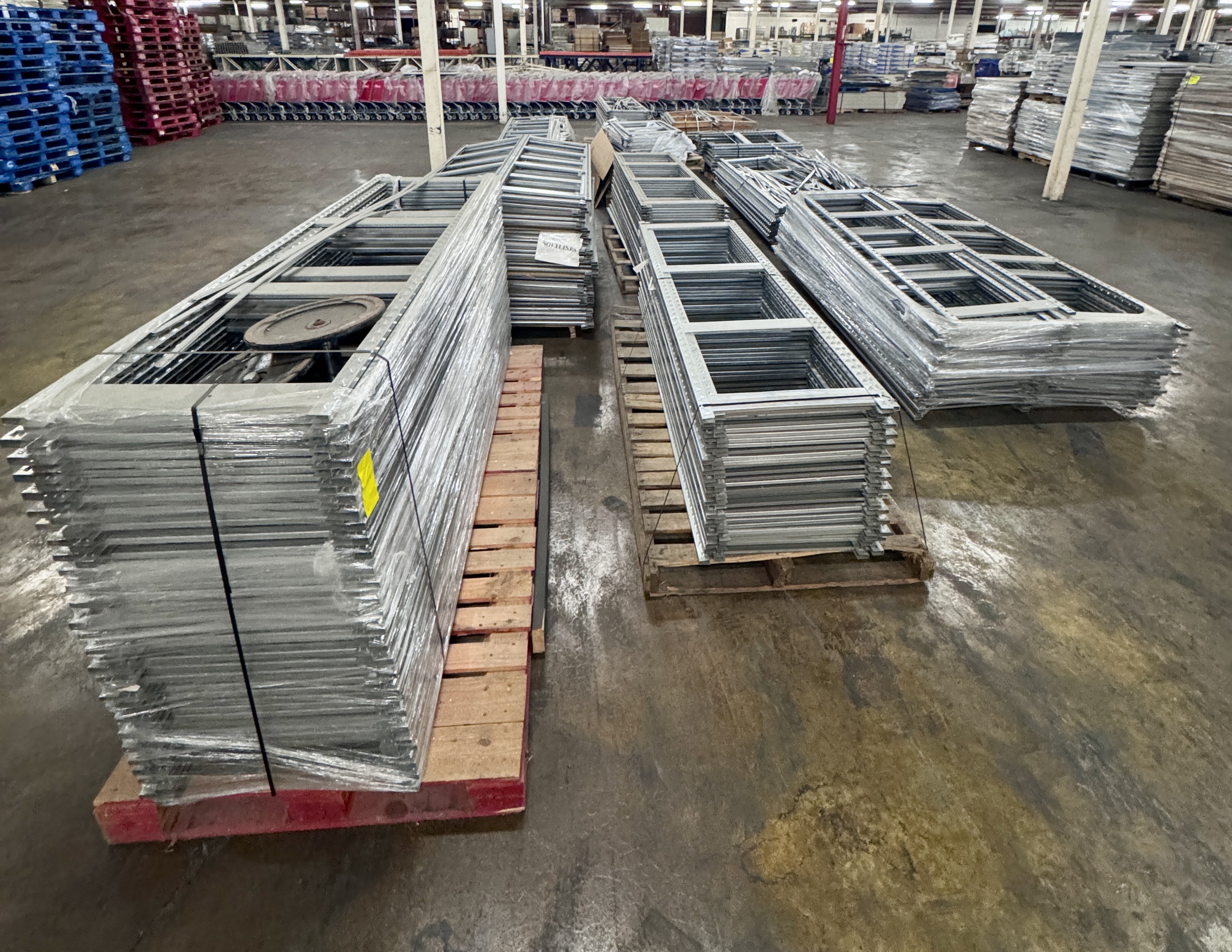 Bulk S-Series backroom shelving uprights and metal frames stacked on pallets inside a warehouse. Heavy-duty stockroom shelving components available from Mid-America Store Fixtures.