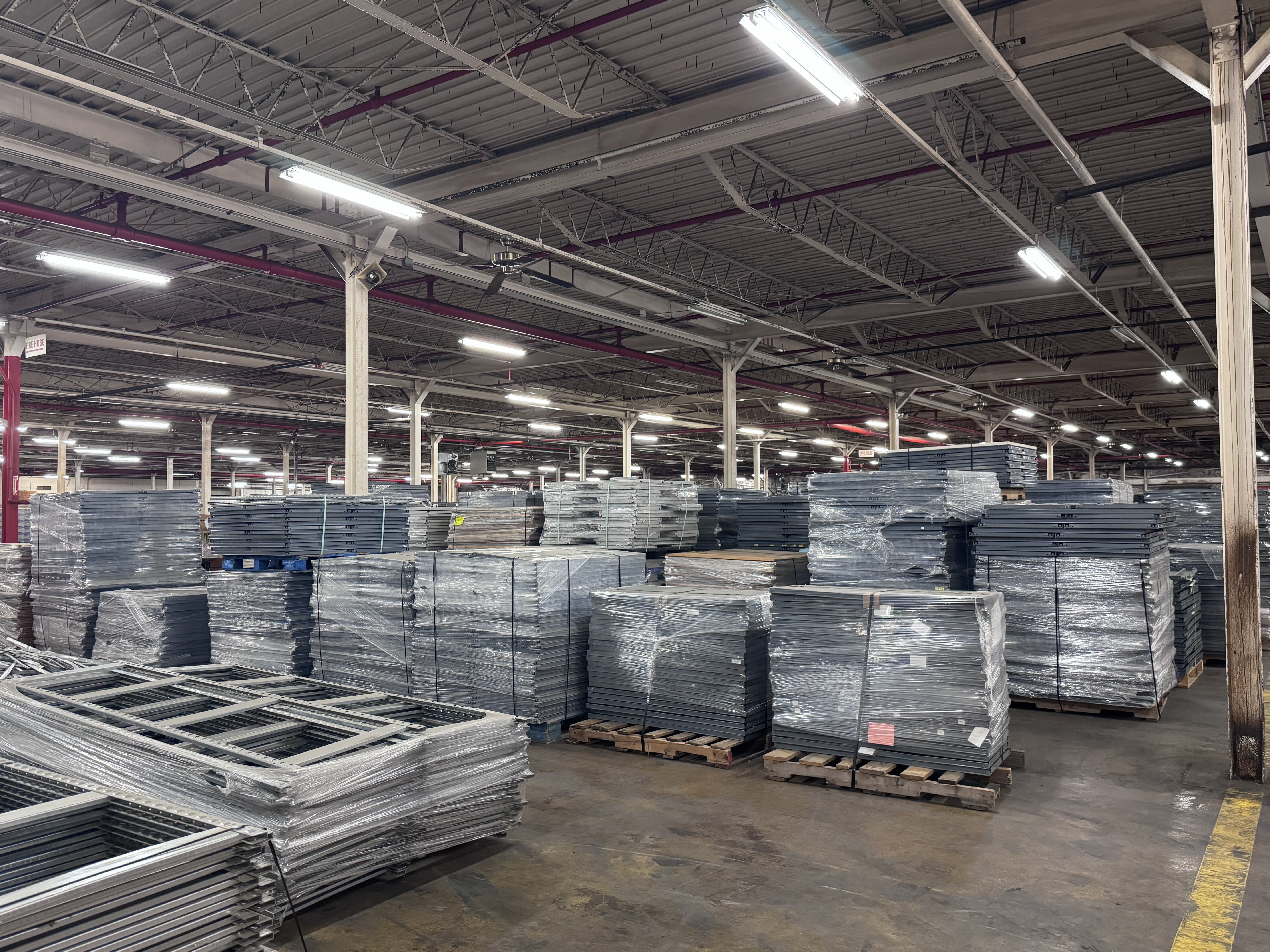 Extensive warehouse inventory of S-Series backroom shelving, including metal shelves and uprights stacked on pallets for high-capacity retail stockroom storage. S-Series shelving available from Mid-America Store Fixtures.
