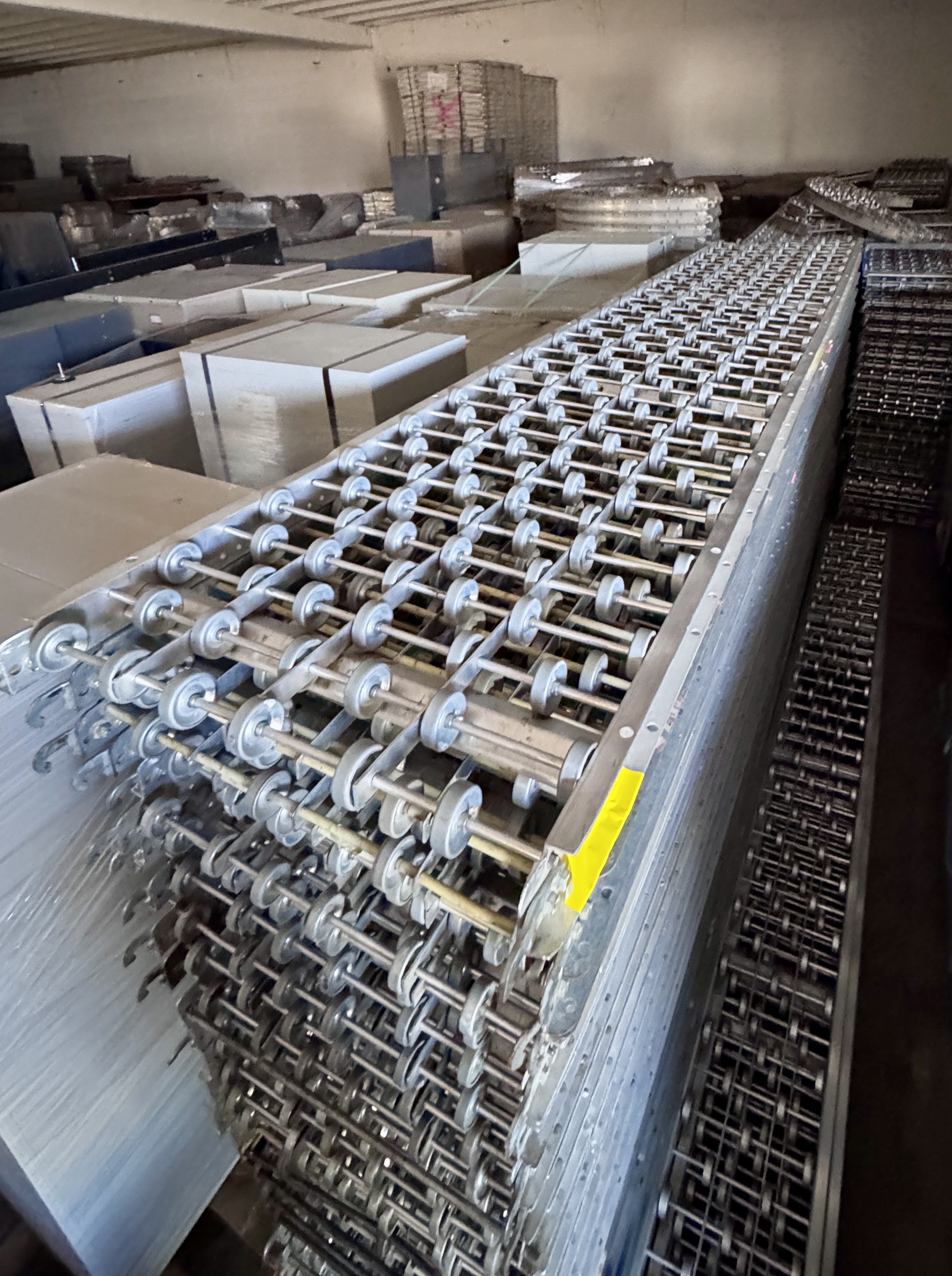 Bulk quantities of metal skate wheel conveyor rails neatly stacked inside a warehouse for retail and warehouse material handling applications. Skate wheel conveyor systems available from Mid-America Store Fixtures.