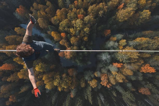 Picture of a man tightroping over the forest 