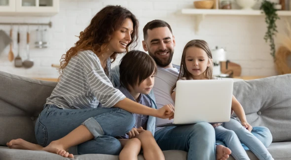 A young family sitting on the couch in their new home, purchased with a Virginia Housing DPA program.