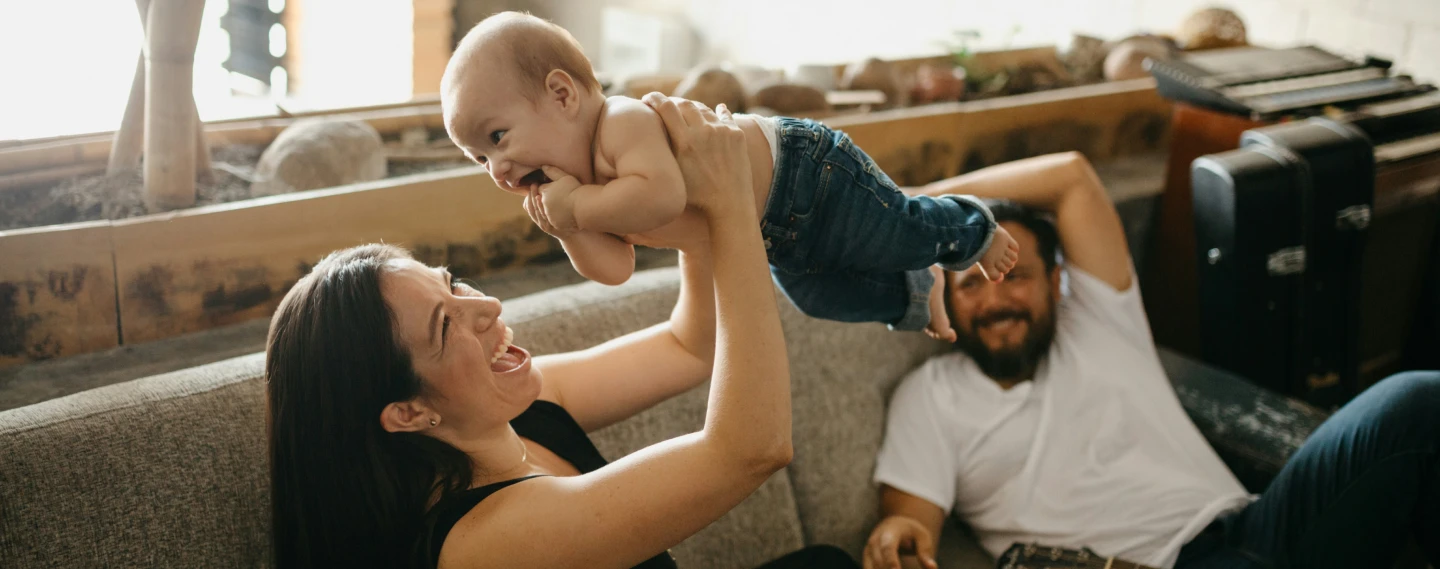 First-time homebuyers playing with their infant son in the living room of their new house.