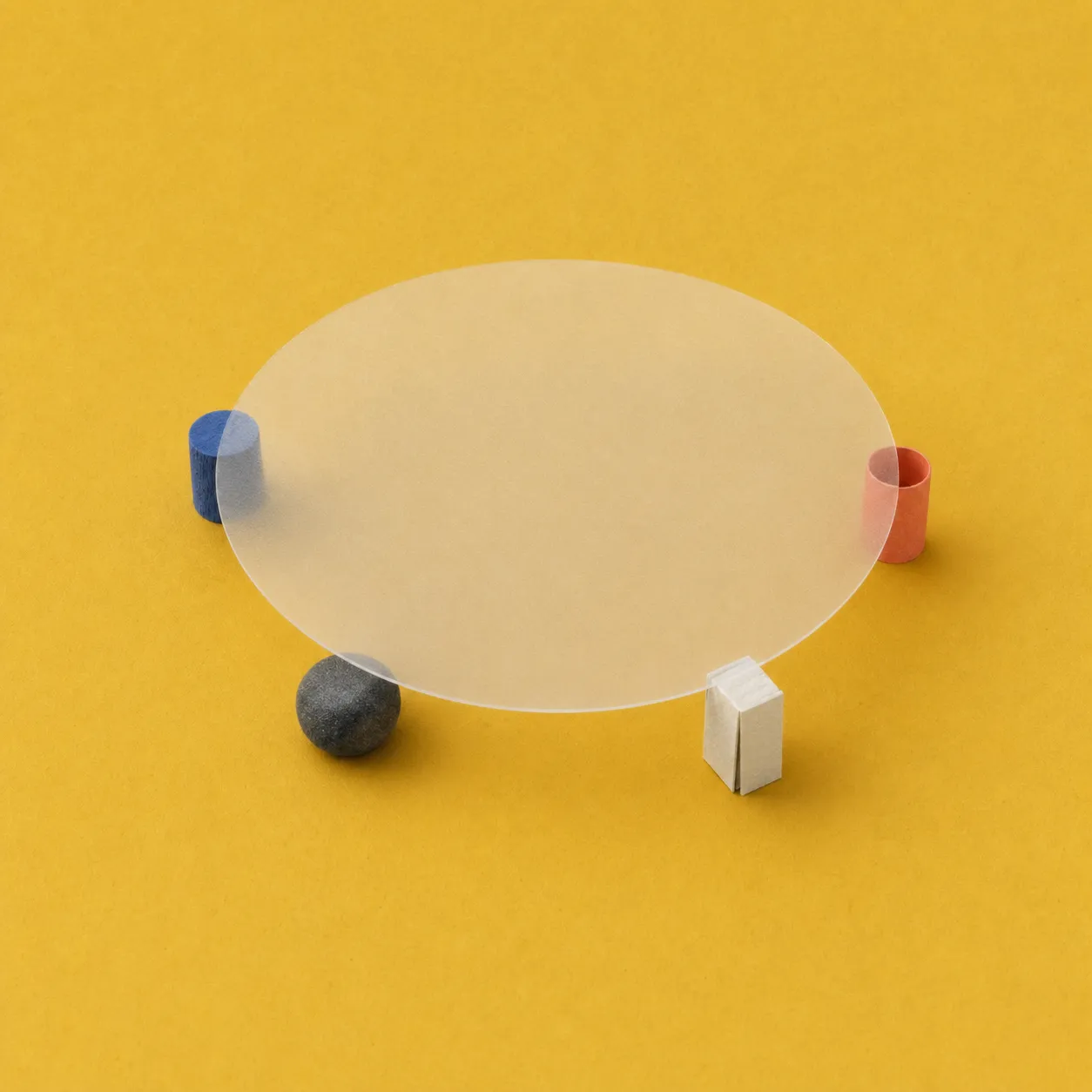 Transparent round glass table supported by four legs: blue cylinder, black sphere, cream rectangle, red cylinder.