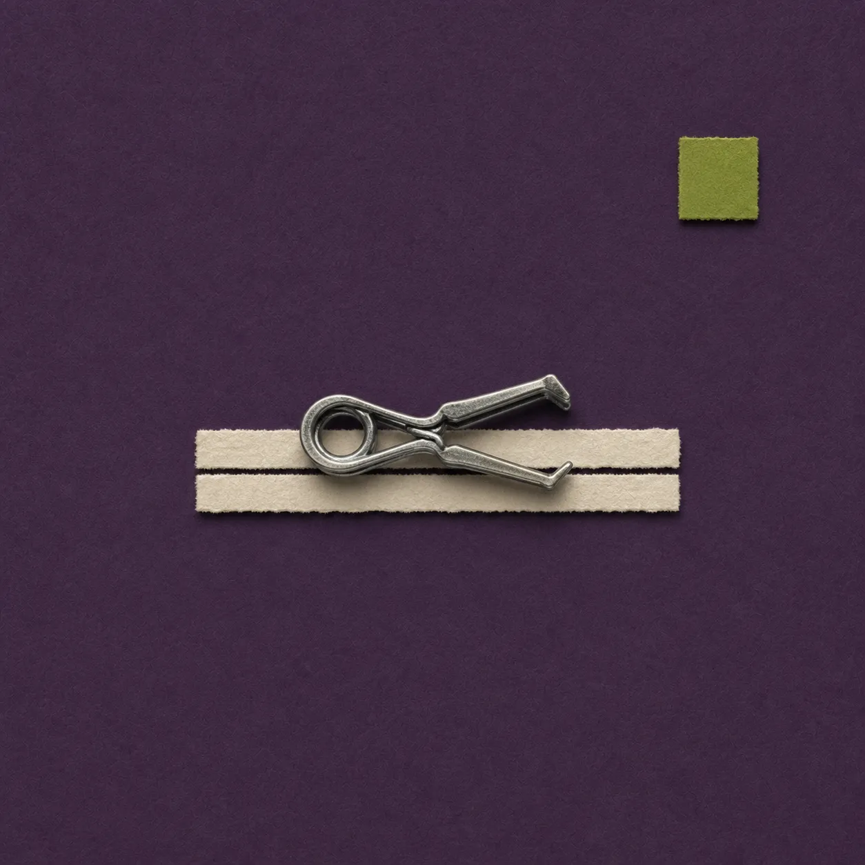 Metal aneurysm clip placed on two torn beige paper strips against a purple background with a green square.