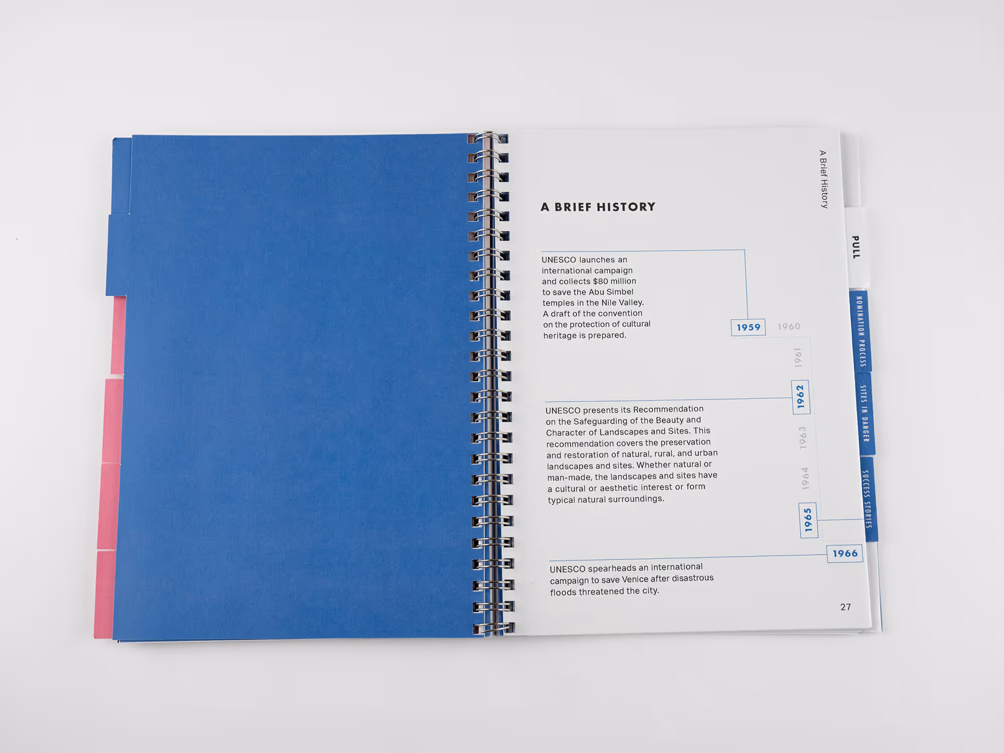 Open spiral-bound book showing a timeline titled 'A Brief History' with UNESCO milestones from 1959 to 1966 and blue and pink tabs on the edges.