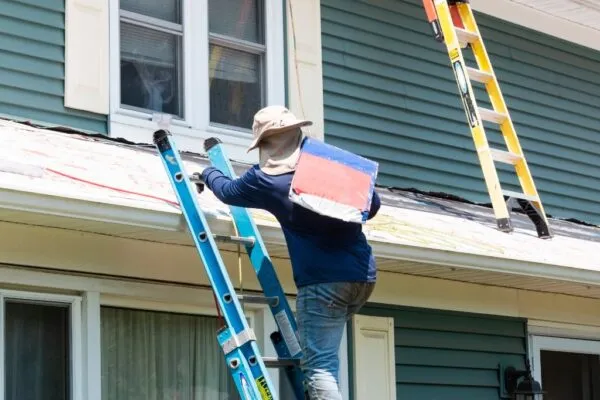 A roofer carrying a bag up on a ladder to the roof