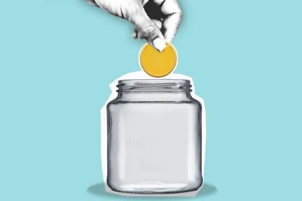 A hand dropping a coin into a jar for a budget
