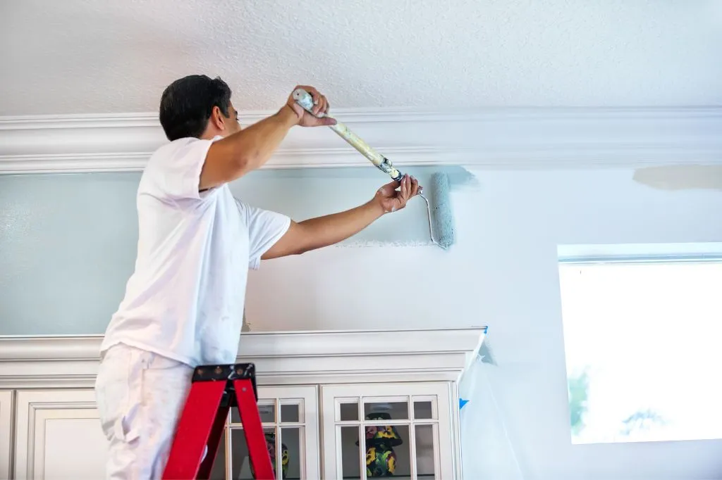 A roofer painting the interior of a home for additional income