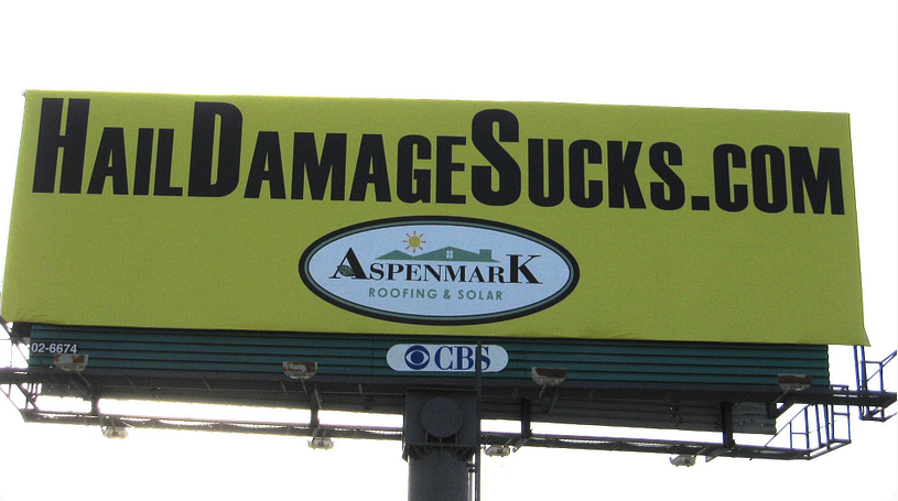 A yellow roofing billboard that says hail damage sucks