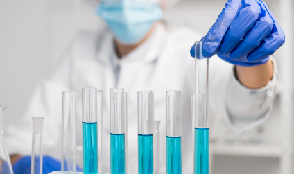 Close-up of lab test tubes filled with blue liquid, handled by a gloved scientist for pest control product testing