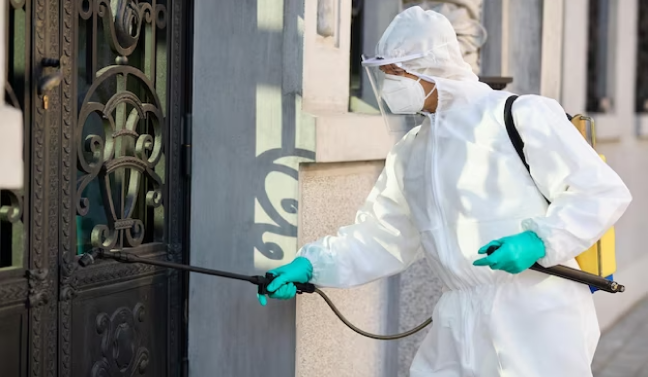 Pest control technician in full protective gear spraying a residential building entrance for pest prevention

