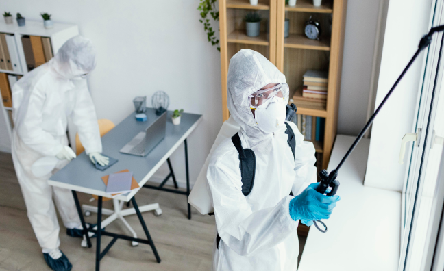 Two licensed pest control technicians in protective suits treating an indoor space for bug infestations

