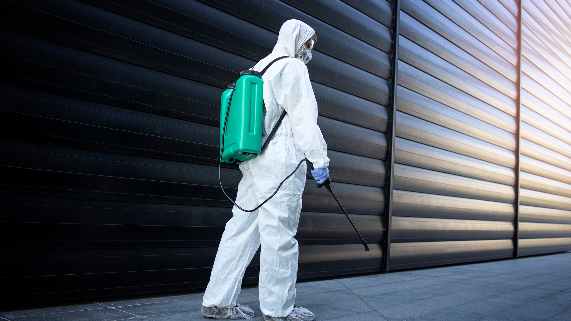 Professional pest control technician in protective gear spraying exterior building walls for pest prevention.
