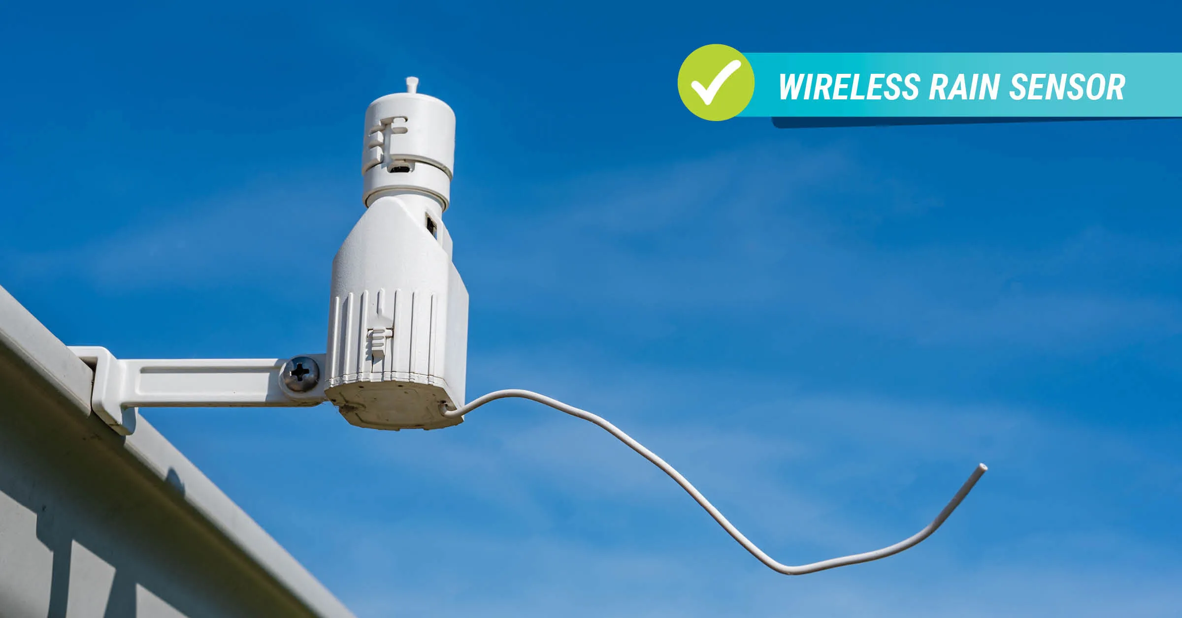 Close-up of a white wireless rain sensor mounted on the edge of a residential roof against a clear blue sky.
