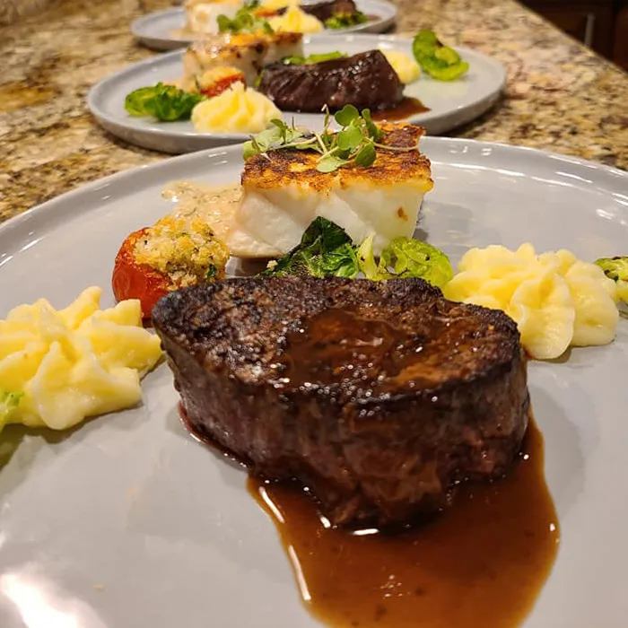 A delicious plate of steak and fish over a bed of vegetables.